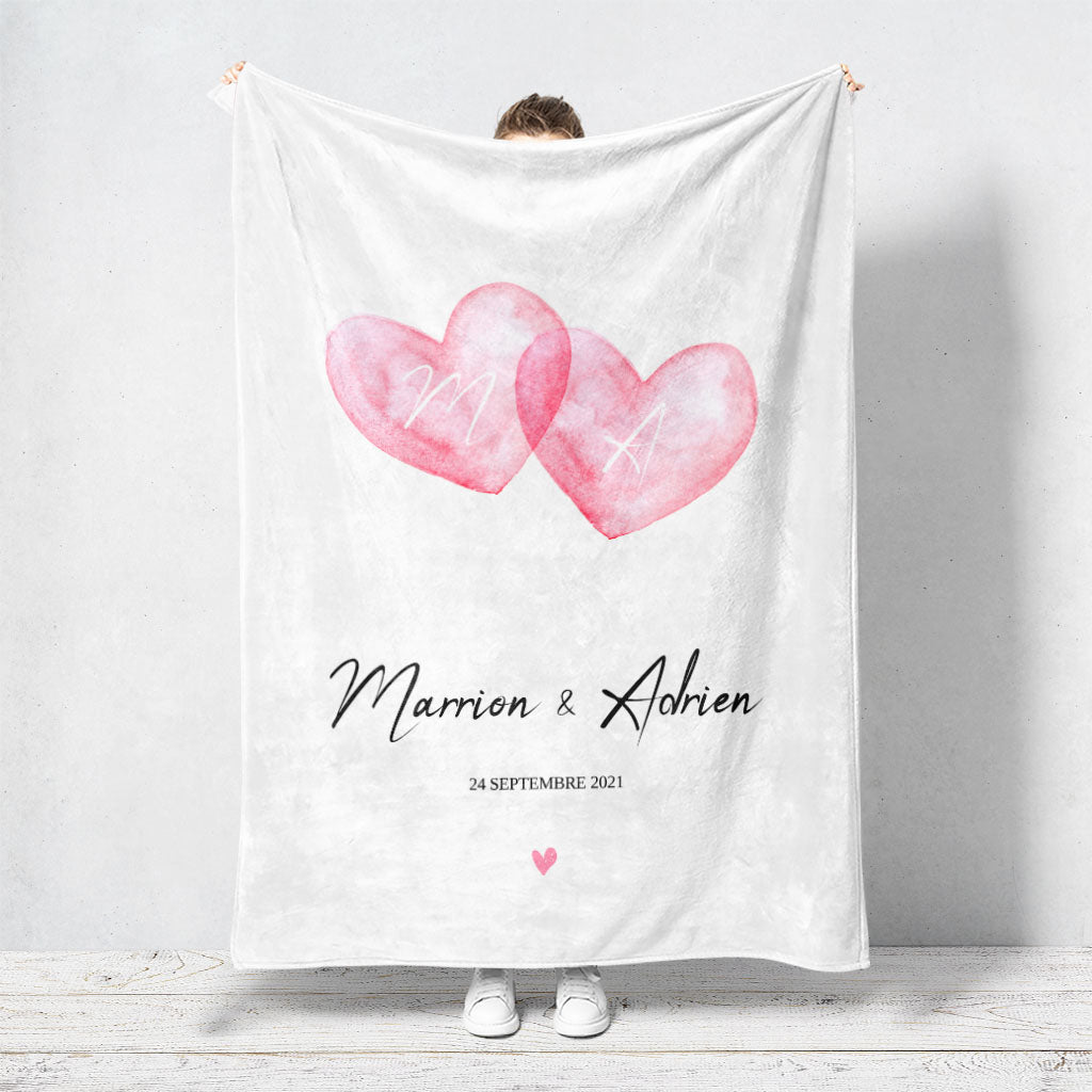 Un plaid personnalisé couple qui représente deux coeurs en aquarelle roses qui se touchent sur un fond blanc. Les prénoms et la date de rencontre du couple sont personnalisables. Le design est minimaliste.