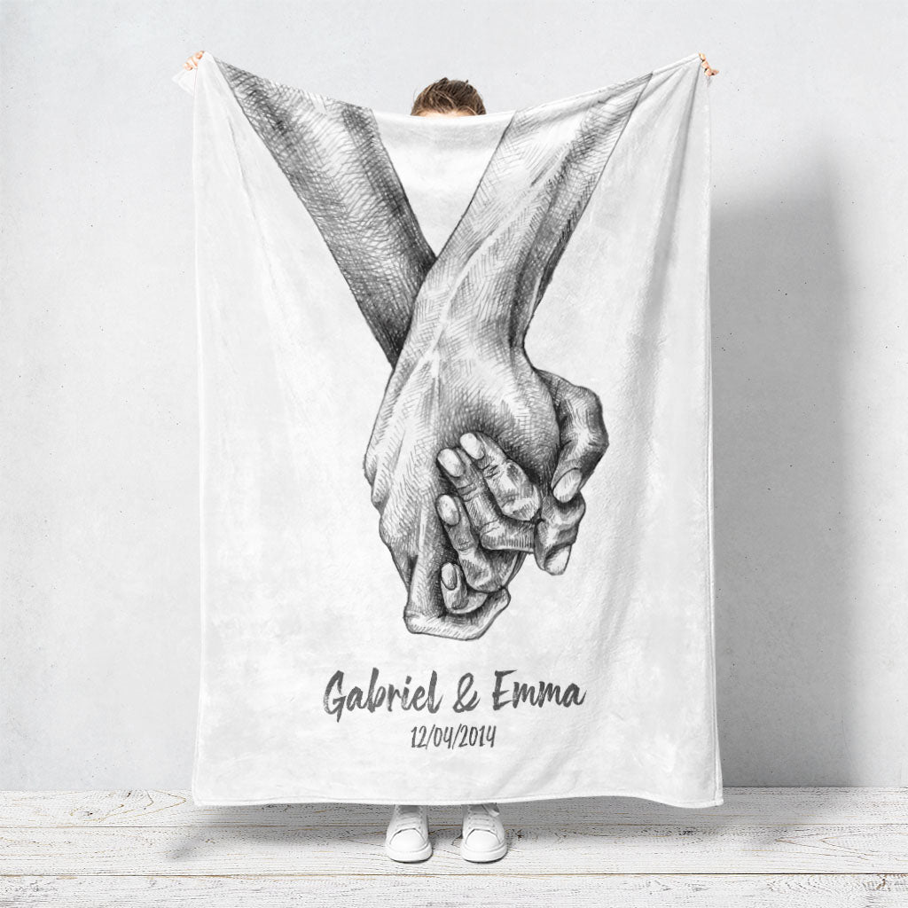 Un plaid personnalisé couple qui représente deux mains qui s’enlacent dessinées au fusain sur un fond blanc. Les prénoms et la date de rencontre du couple sont personnalisables. Le design est minimaliste.