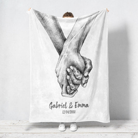 Un plaid personnalisé couple qui représente deux mains qui s’enlacent dessinées au fusain sur un fond blanc. Les prénoms et la date de rencontre du couple sont personnalisables. Le design est minimaliste.