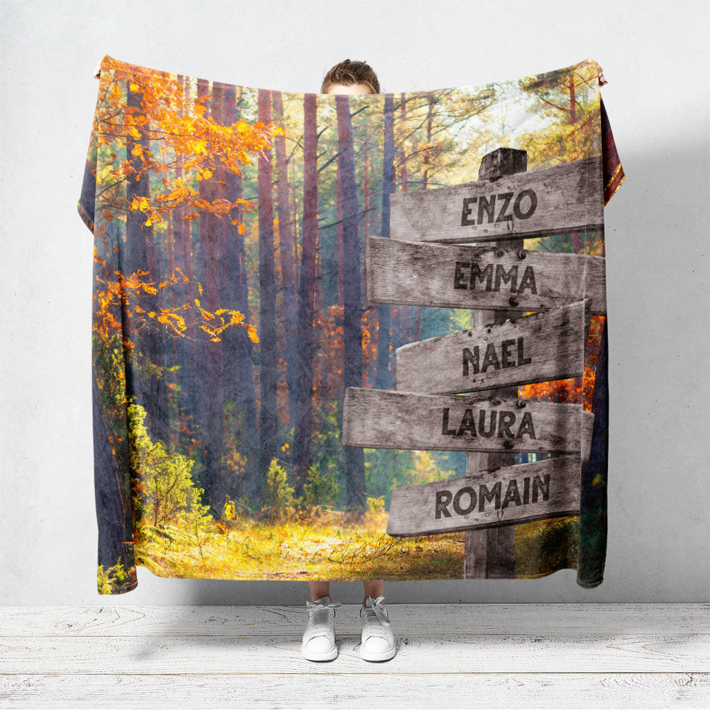 Un plaid personnalisé famille qui représente des panneaux de direction en bois avec des prénoms inscrit dessus en plein forêt d’automne. Les prénoms sur les panneaux sont personnalisables.