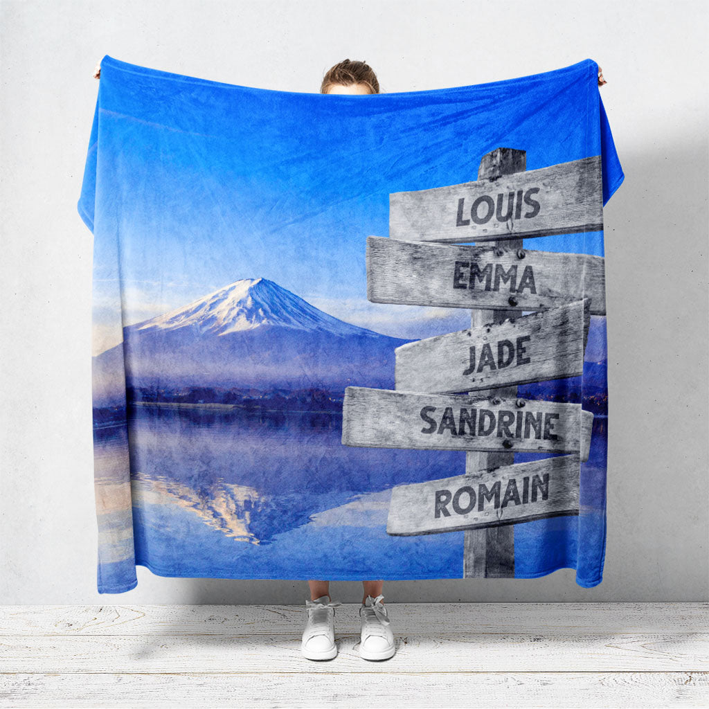 Un plaid personnalisé famille qui représente des panneaux de direction en bois avec des prénoms inscrit dessus au bord d'une rivière avec le mont Fuji visible au Japon. Les prénoms sur les panneaux sont personnalisables.