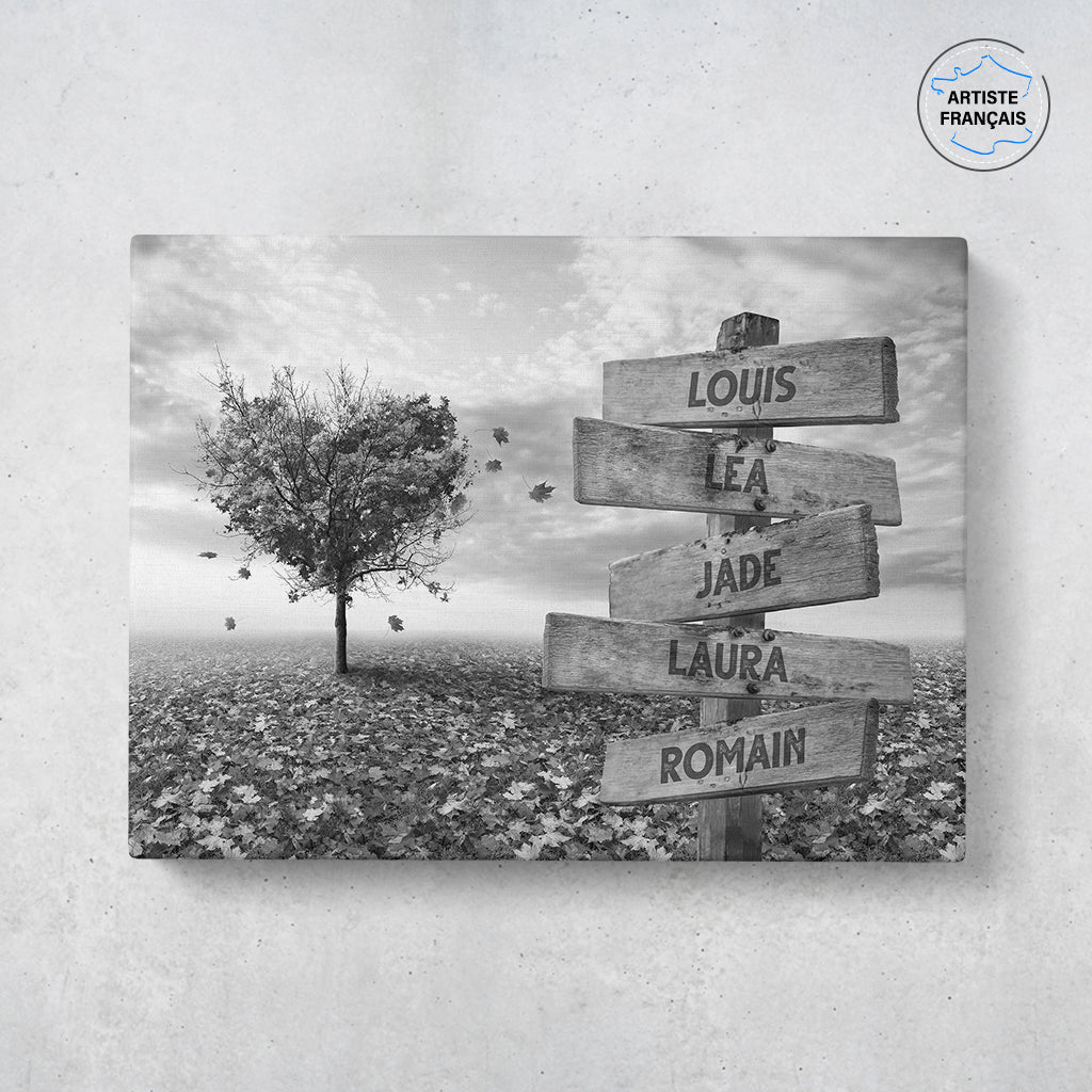 Un tableau personnalisé famille qui représente des panneaux de direction en bois avec des prénoms inscrit dessus dans un champs recouvert de feuilles en automne avec un arbre en forme de coeur. Le design est en noir et blanc. Les prénoms sur les panneaux sont personnalisables.