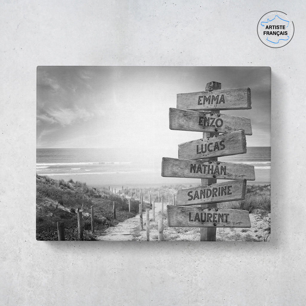Un tableau personnalisé famille qui représente des panneaux de direction en bois avec des prénoms inscrit dessus, au bord d’une plage et son coucher de soleil en noir et blanc. Les prénoms sur les panneaux sont personnalisables.