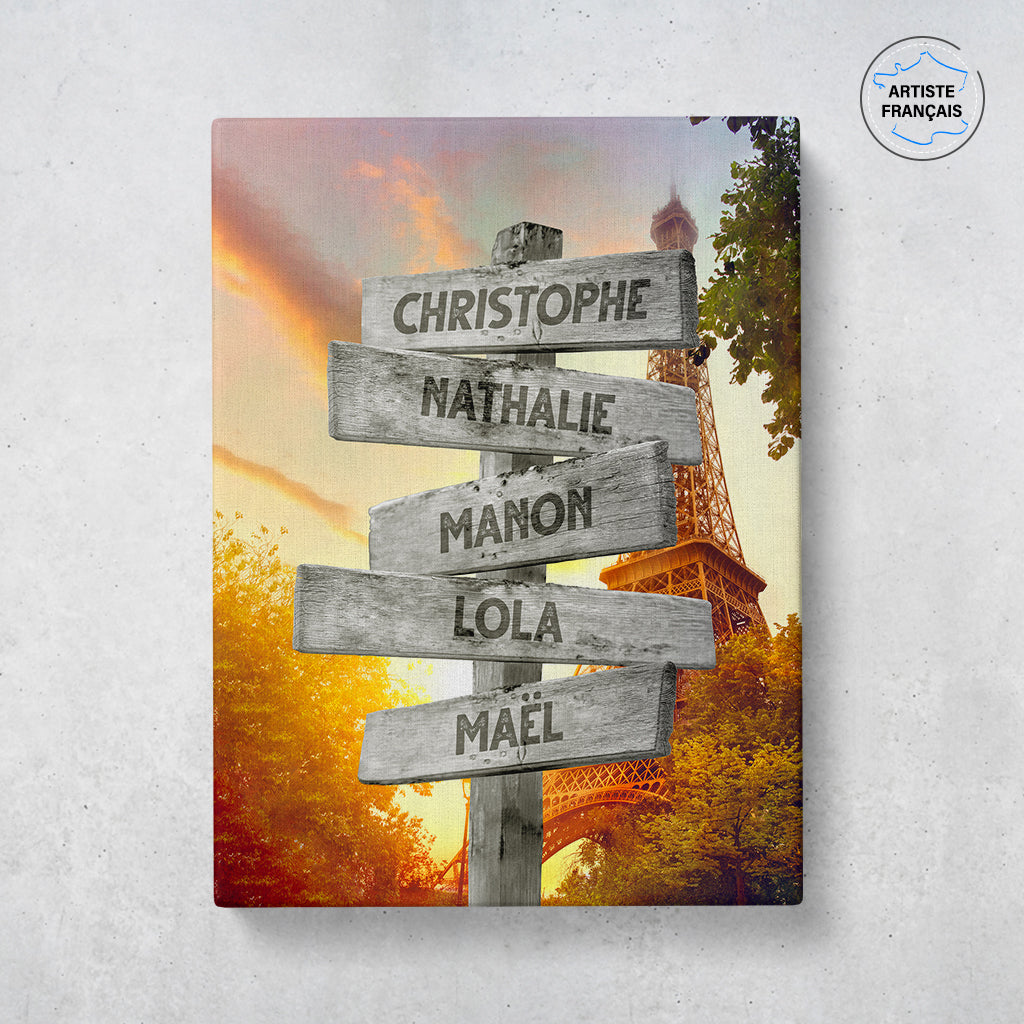 Un tableau personnalisé famille qui représente des panneaux de direction en bois avec des prénoms inscrit dessus dans la ville de Paris avec la Tour Eiffel sous un magnifique coucher de soleil. Les prénoms sur les panneaux sont personnalisables.