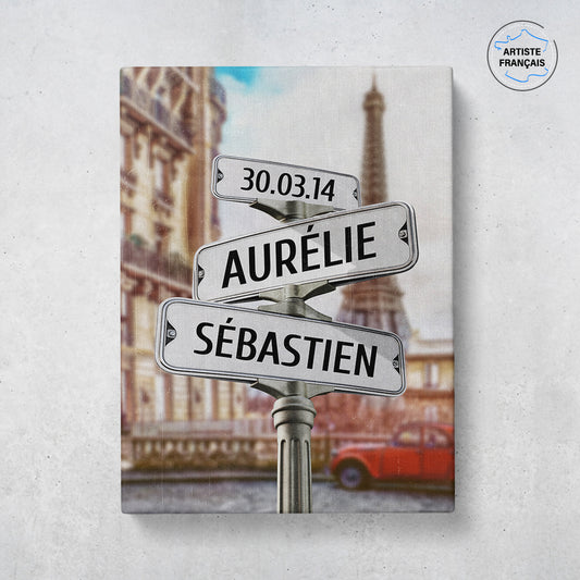 Un tableau personnalisé couple qui représente des panneaux de direction dans la vielle ville de Paris avec la tour Eiffel et une ancienne 2 cheveux Citroën rouge. Les prénoms et dates de naissances sur les panneaux sont personnalisables.