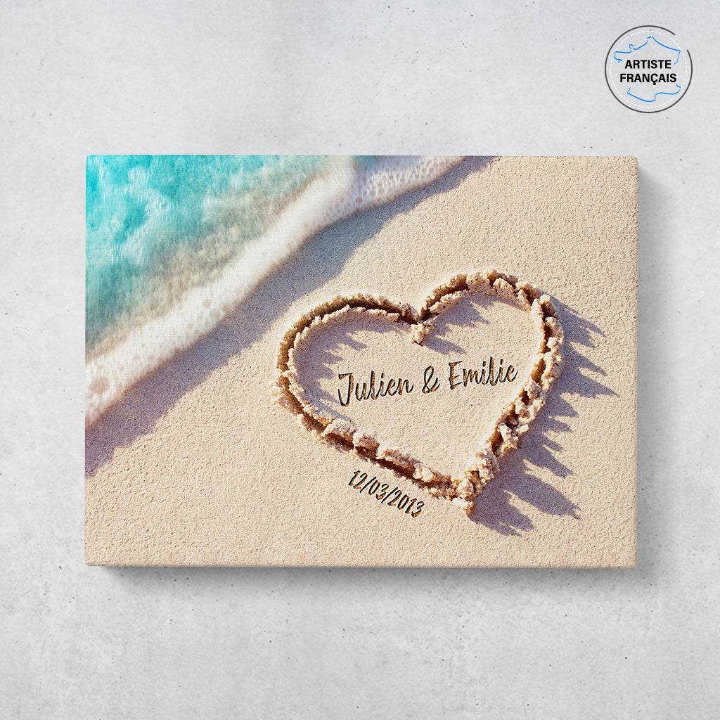 Un tableau personnalisé couple qui représente un coeur dessiné dans le sable d’une plage avec les prénoms du couple et leur date de rencontre . Les prénoms et la date de rencontre du couple sont personnalisables.