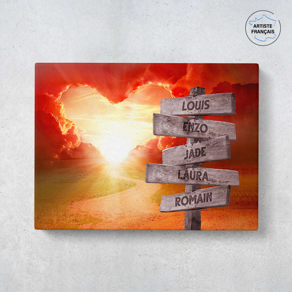 Un tableau personnalisé famille qui représente des panneaux de direction en bois avec des prénoms inscrit dessus planté au bord d'un chemin menant à un coeur nuageux et un coucher de soleil. Les prénoms sur les panneaux sont personnalisables.