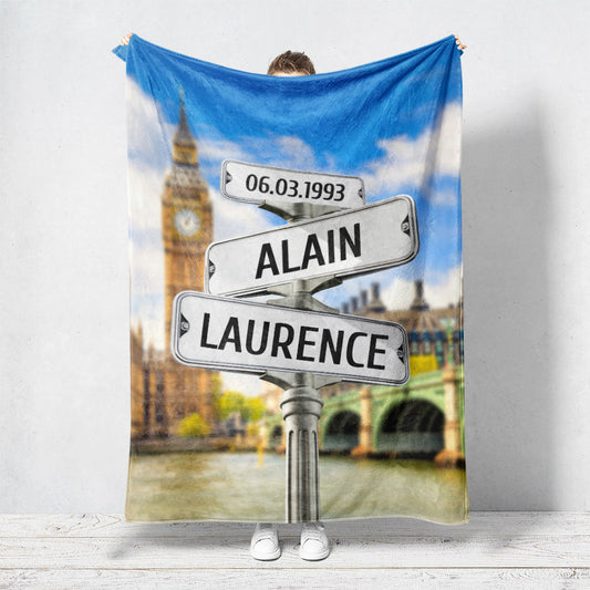 Un plaid personnalisé couple représentant des panneaux de direction de la ville de Londres avec Big Ben en arrière plan. Les prénoms du couple, la date de rencontre et les textes sont personnalisables.