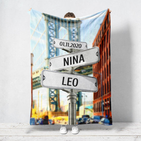 Un plaid personnalisé couple qui représente des panneaux de direction de la ville de New York, face à l’un de ses mythiques ponts. Les prénoms et dates de naissances sur les panneaux sont personnalisables.