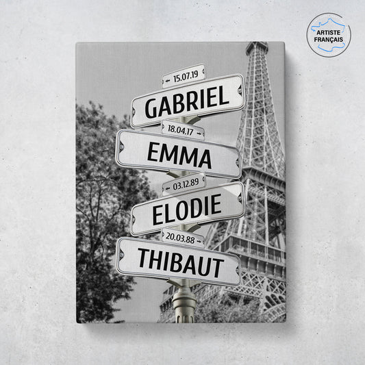 Un tableau personnalisé famille qui représente des panneaux de direction de la ville de Paris avec la tour Eiffel et un arbre en noir et blanc. Les prénoms et dates de naissances sur les panneaux sont personnalisables.