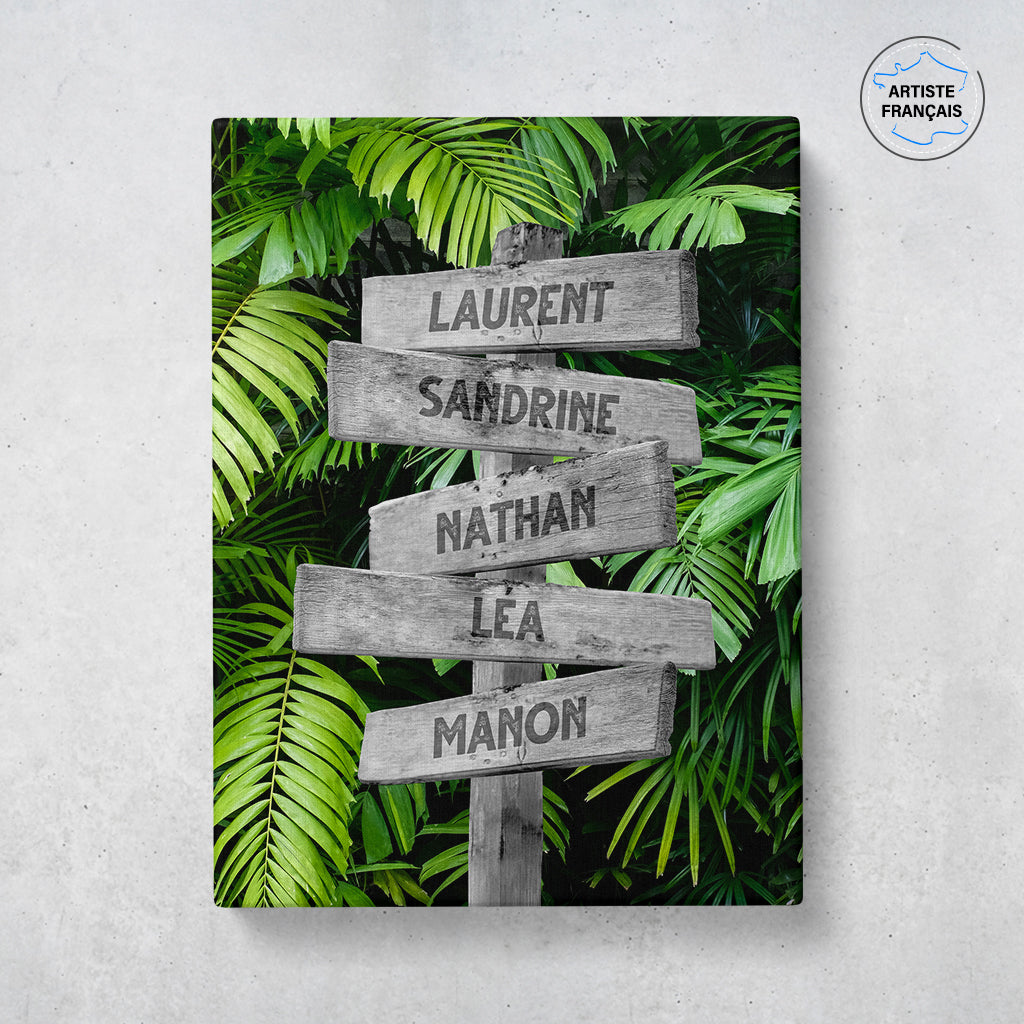 Un tableau personnalisé famille qui représente des panneaux de direction en bois avec des prénoms inscrit dessus dans un décors de forêt tropicale avec de grosses feuilles vertes. Les prénoms sur les panneaux sont personnalisables.