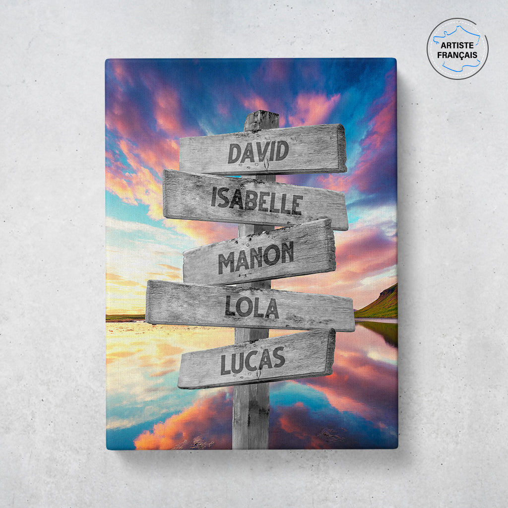 Un tableau personnalisé famille qui représente des panneaux de direction en bois avec des prénoms inscrit dessus dans un décors de lac qui reflète des nuages multicolores avec un coucher de soleil. Les prénoms sur les panneaux sont personnalisables.
