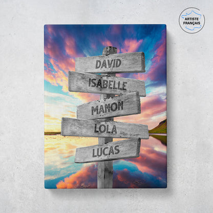 Un tableau personnalisé famille qui représente des panneaux de direction en bois avec des prénoms inscrit dessus dans un décors de lac qui reflète des nuages multicolores avec un coucher de soleil. Les prénoms sur les panneaux sont personnalisables.